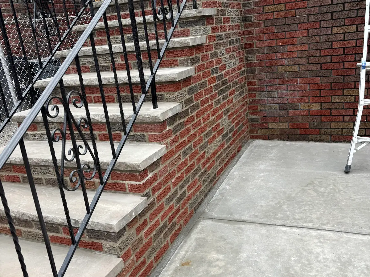 New brick steps with concrete treads and a black iron railing next to a poured concrete pad