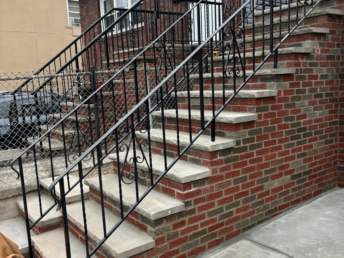 New brick steps with concrete treads and a black iron railing beside a house