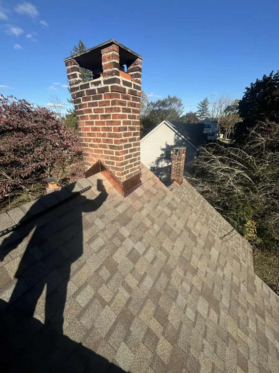 A brick chimney standing above a shingle roof against a clear sky after repair