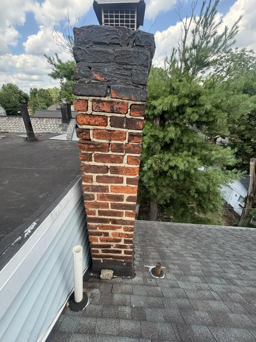 An old brick chimney with the brickwork broken down and the mortar washed out