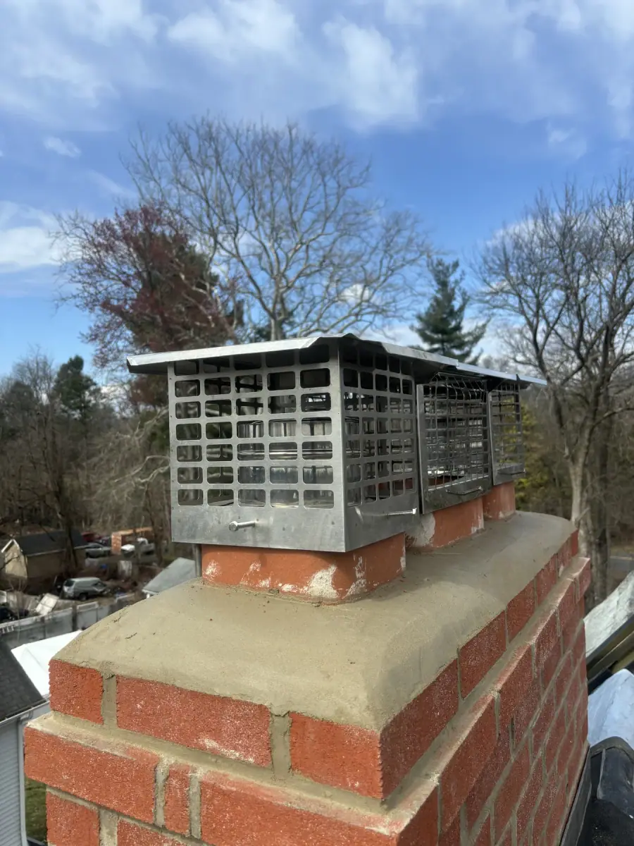 A large metal cap fitted over the crown of a parged brick chimney