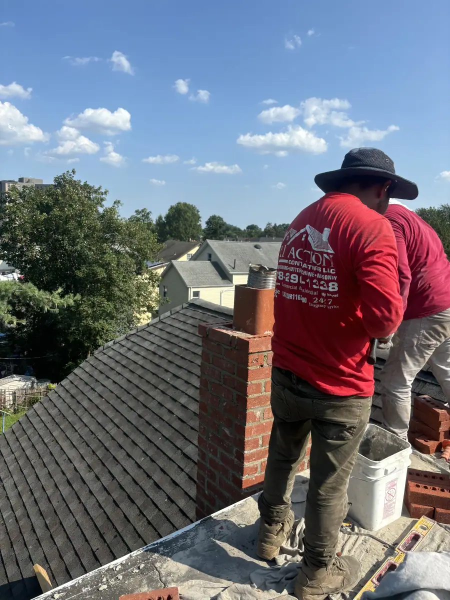 A crew member in a red A1 Action shirt working on a part built brick chimney above a shingle roof