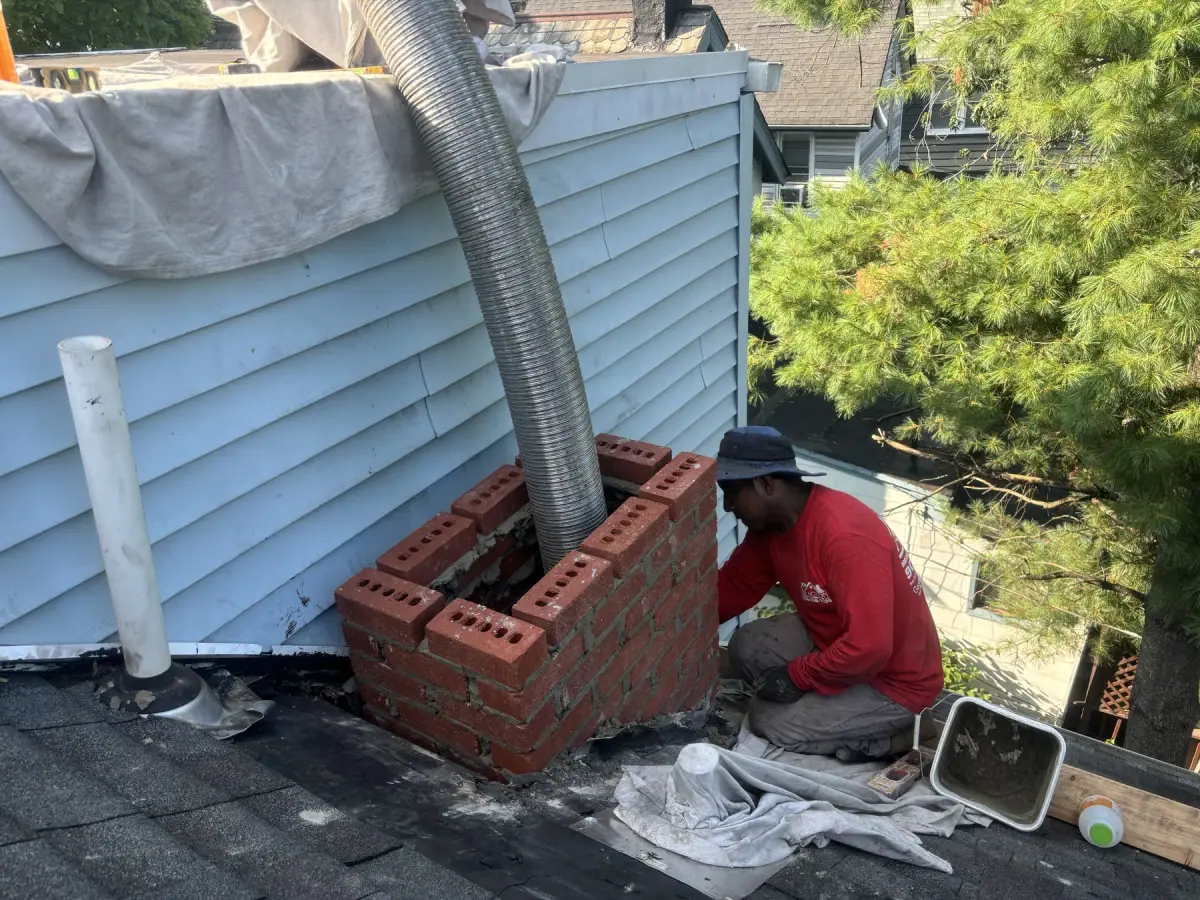 A crew member in a red A1 Action shirt laying new brick on a rebuilt chimney