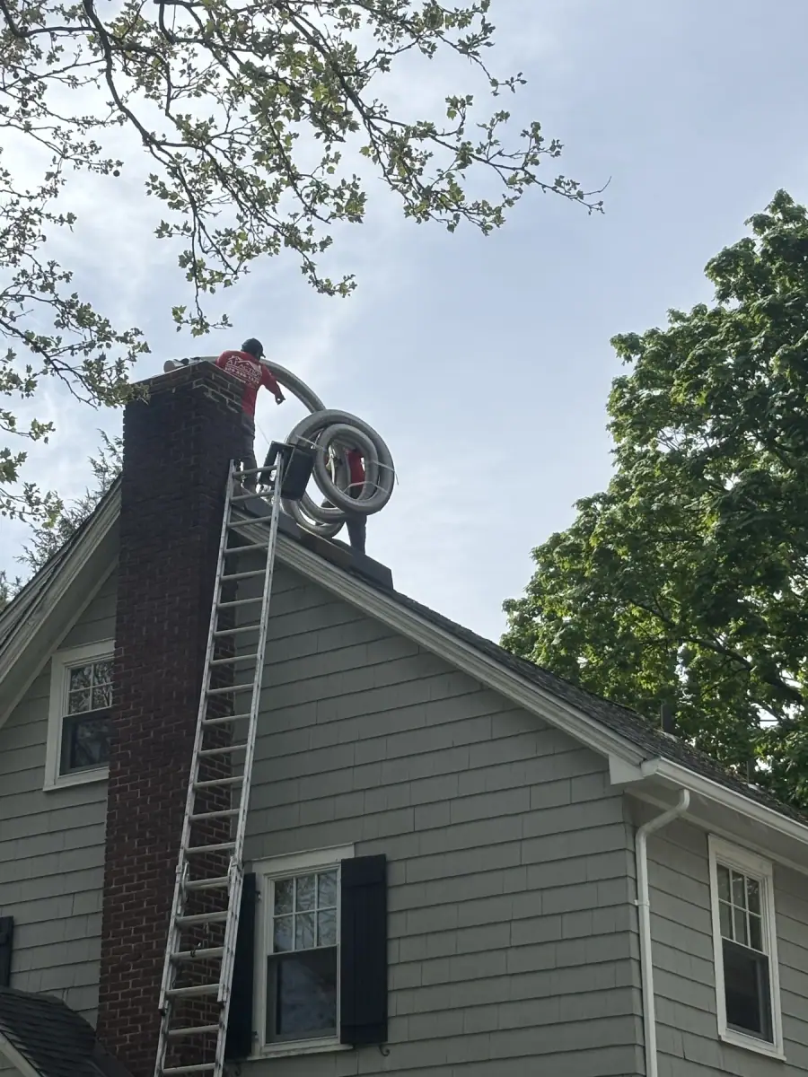 A crew member at the top of a ladder feeding a coiled flexible liner into a brick chimney