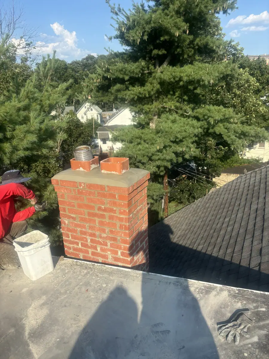 A newly built brick chimney with a fresh crown and two clay flues standing above the roof