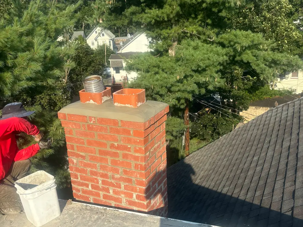 A rebuilt brick chimney on a shingle roof with a crew member working alongside it