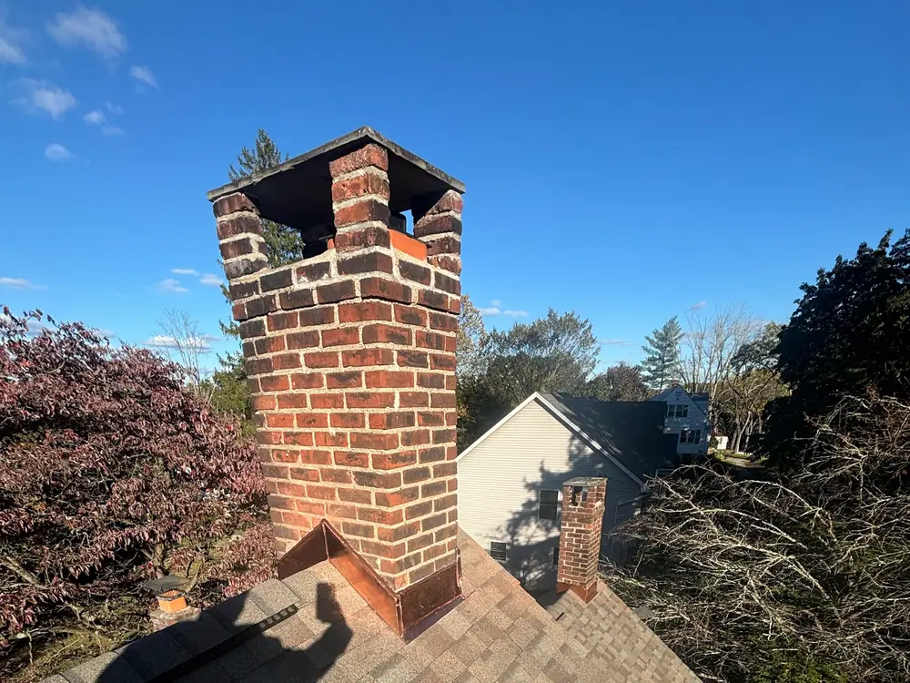 A tall rebuilt brick chimney standing against a clear blue sky above a shingle roof