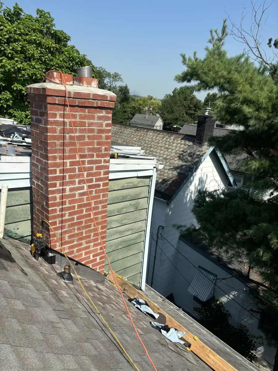 A finished chimney rebuilt in new red brick standing above a roof against the trees