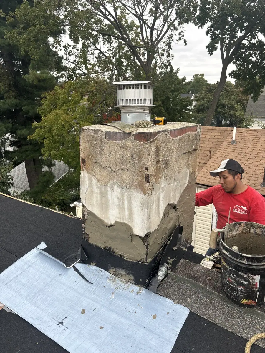 A crew member in a red shirt working on a damaged chimney from a flat roof