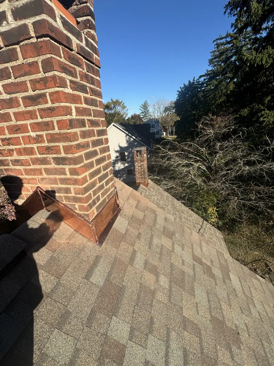 A brick chimney close up with the mortar joints freshly repointed, roof shingles below