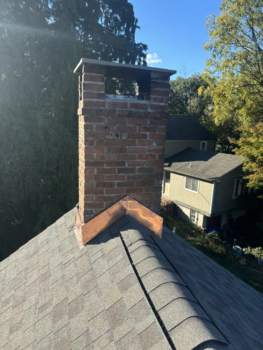 A tall brick chimney with new metal flashing worked in where it passes through the shingles