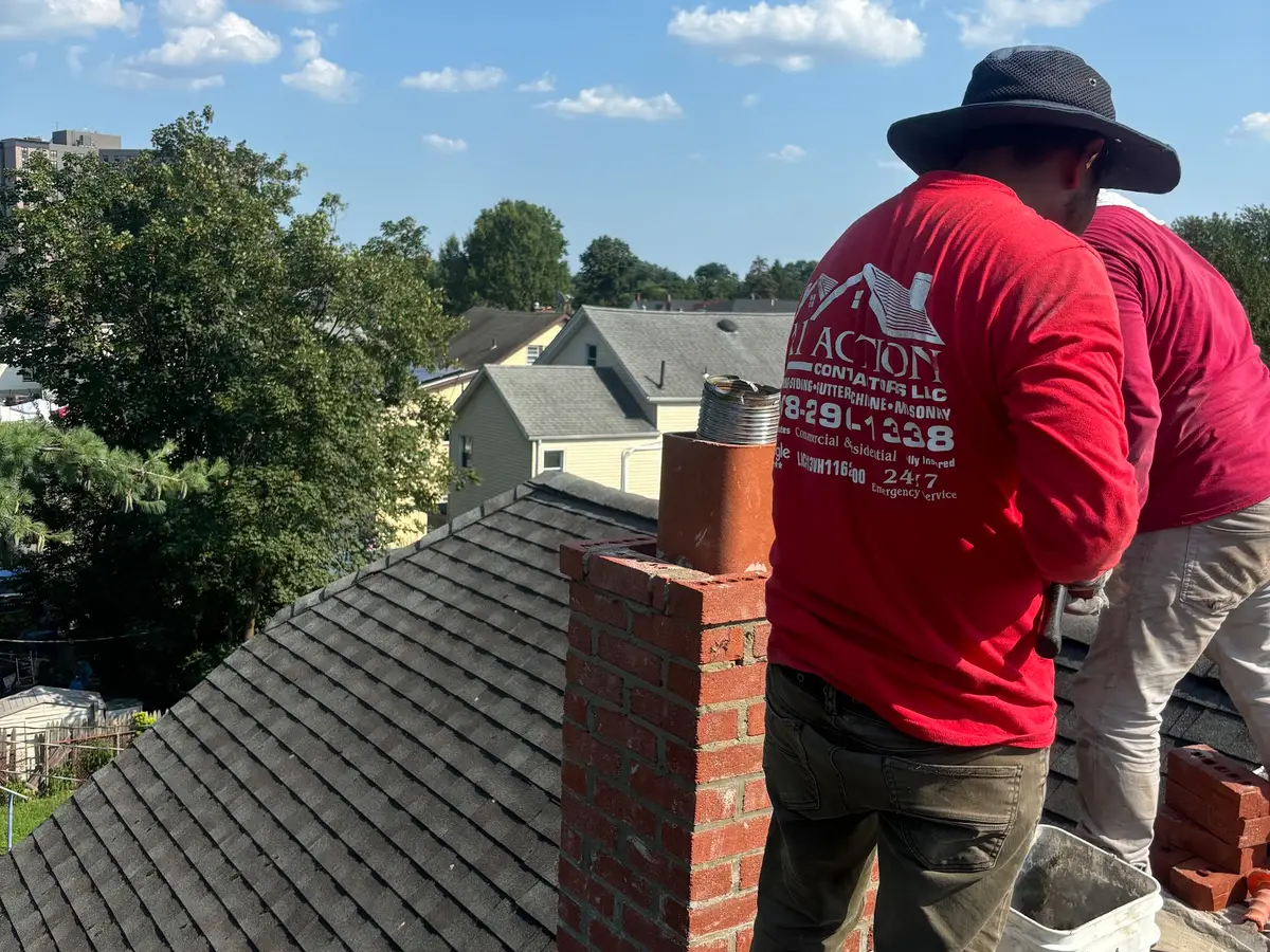 Two A1 Action crew members in red shirts working on a brick chimney on a shingle roof