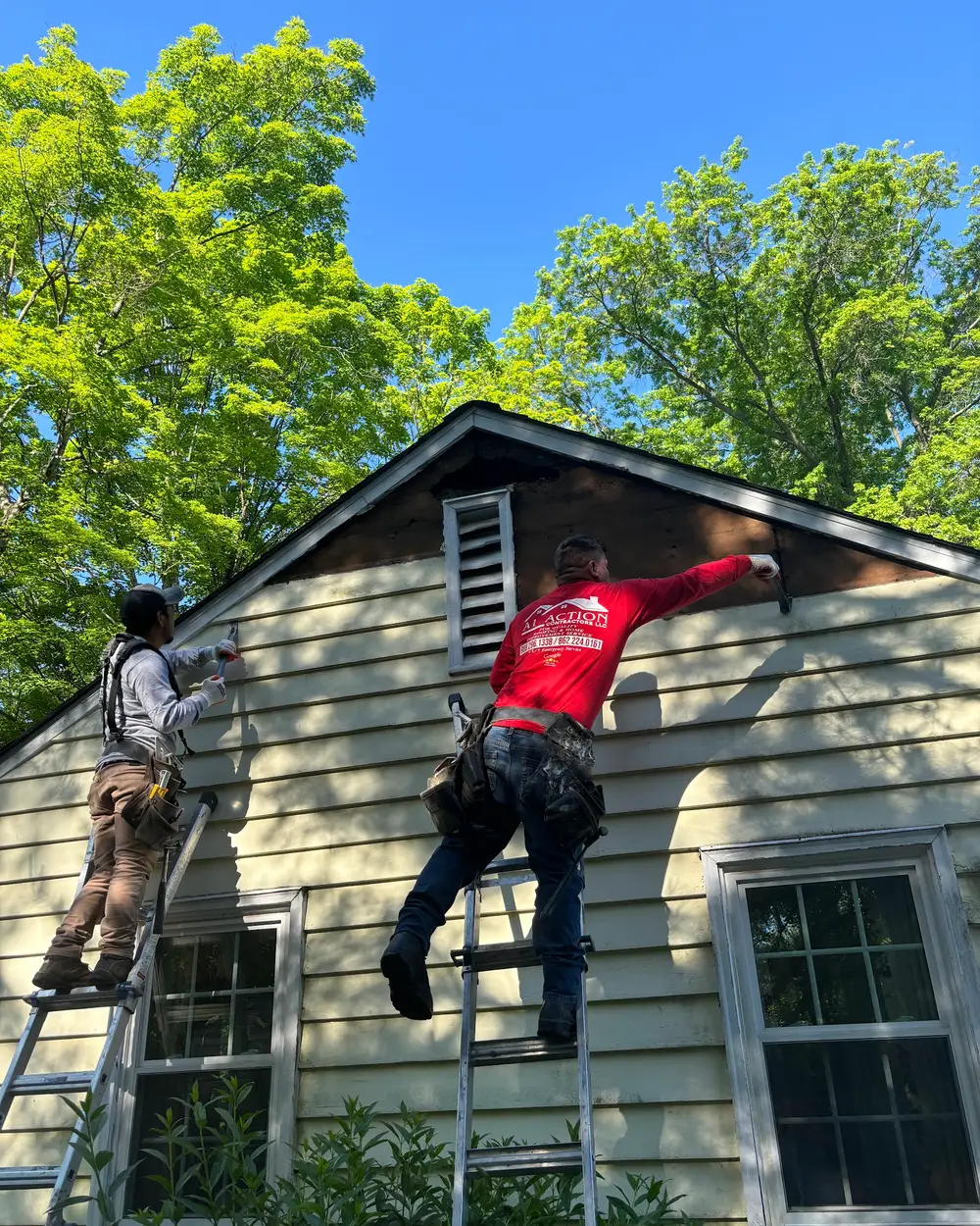 Two A1 Action crew members on ladders fitting siding to the upper wall of a house