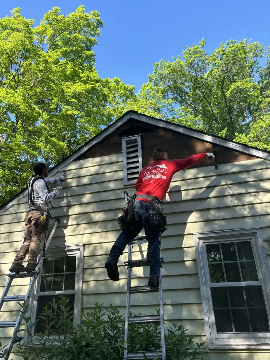 Two crew members in red A1 Action shirts working from ladders at the gable end of a house