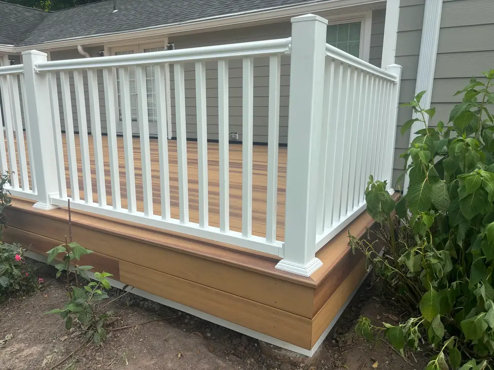 A white deck railing above finished tan skirting, with planting alongside