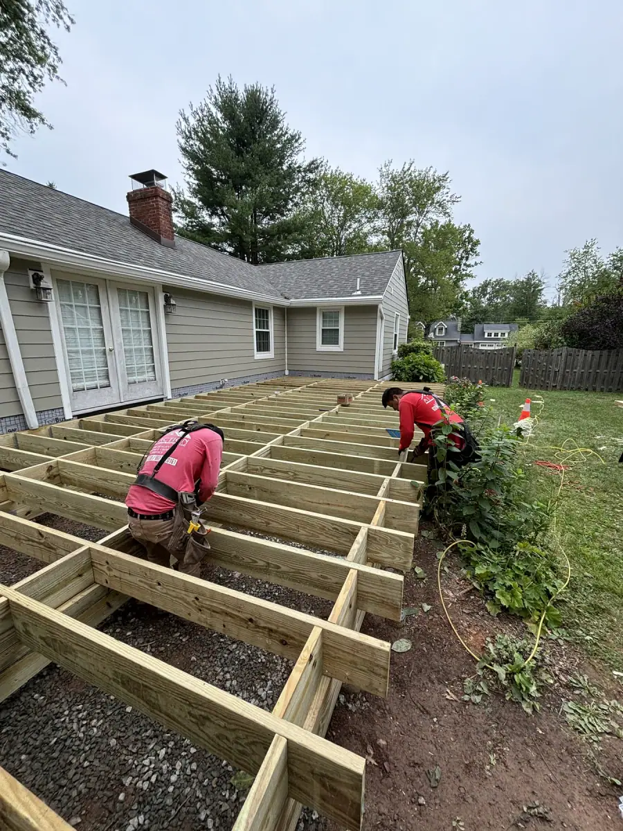 A pressure treated deck frame built out from the back of a house, a crew member fastening joists