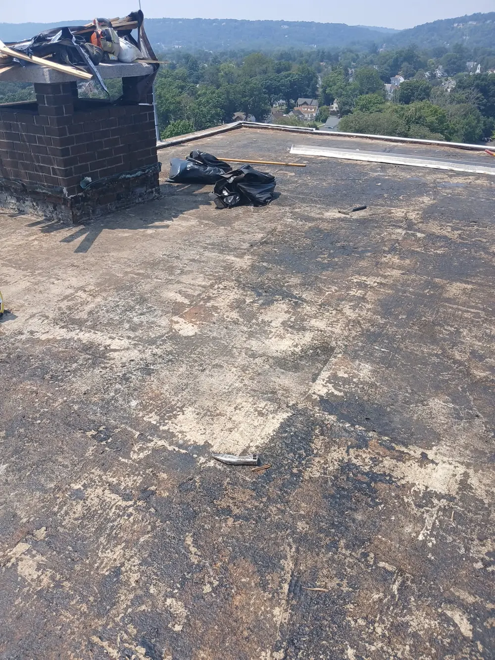 A worn flat roof surface patched and blistered, with an old chimney at the edge, before work began