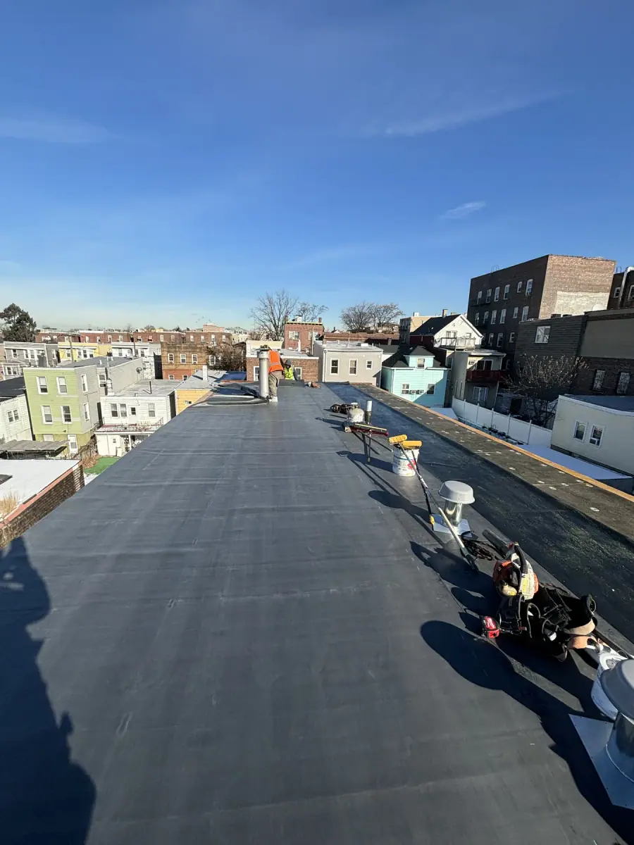 A finished flat roof in black membrane with vents, looking out over city rooftops