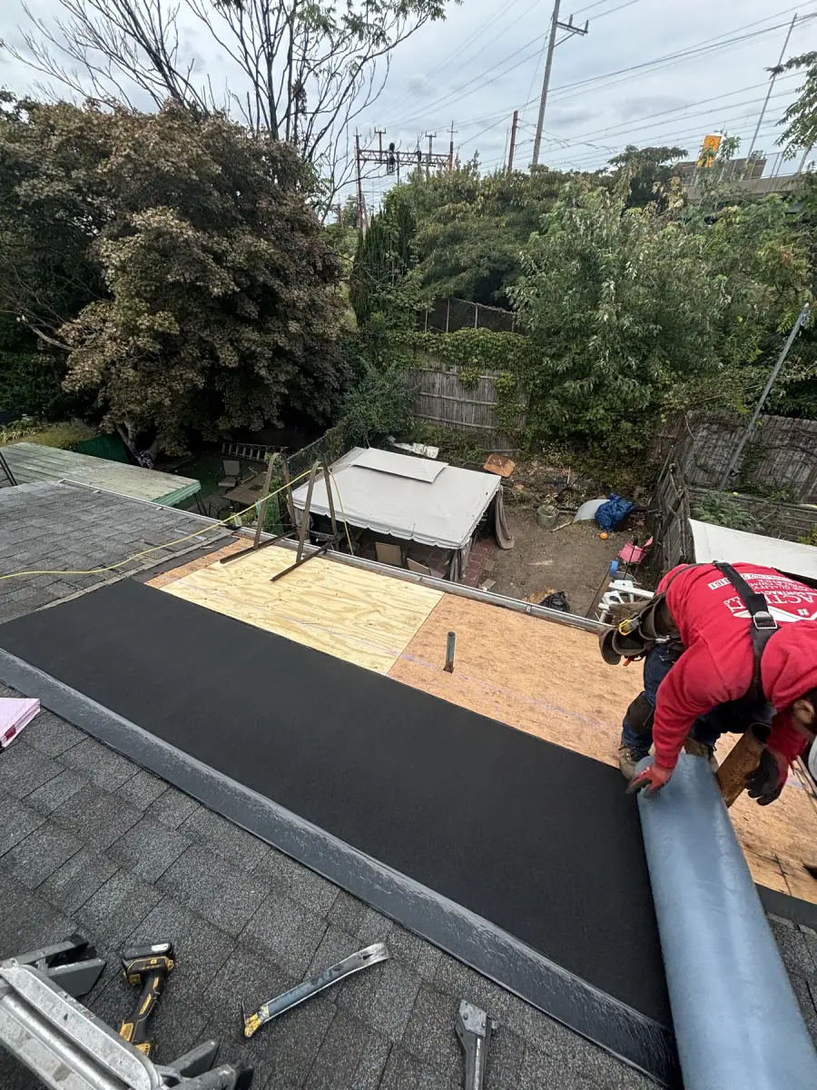 A crew member in a red shirt rolling membrane out over freshly laid plywood on a low roof