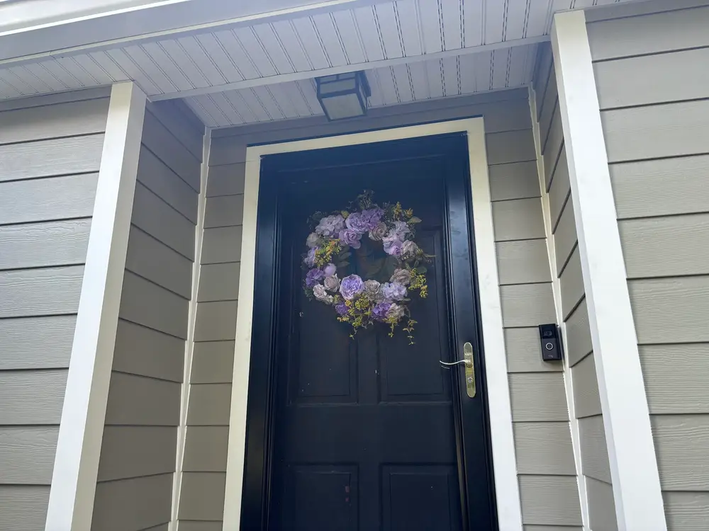 A navy front door with a wreath, framed by newly fitted siding and white trim