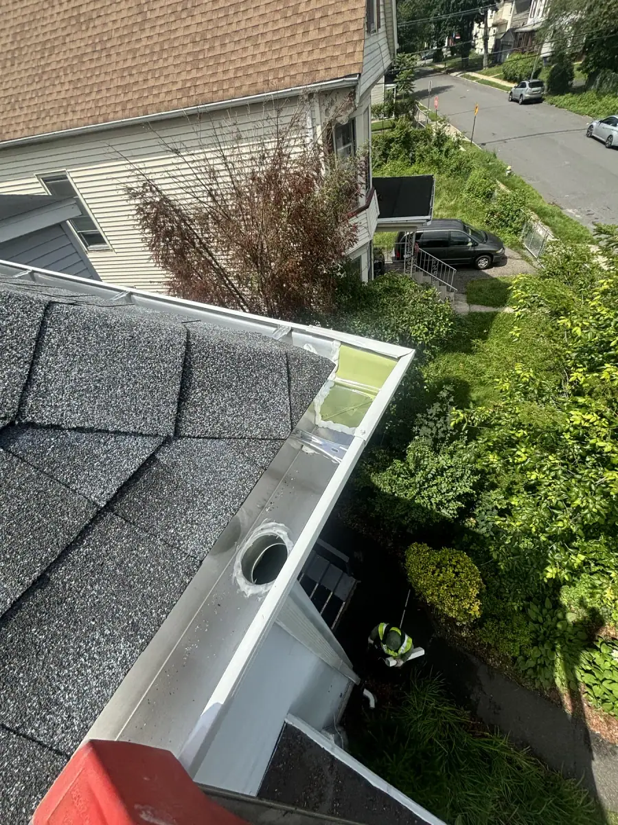 A new gutter and downspout fitted at the corner of a roof above the garden