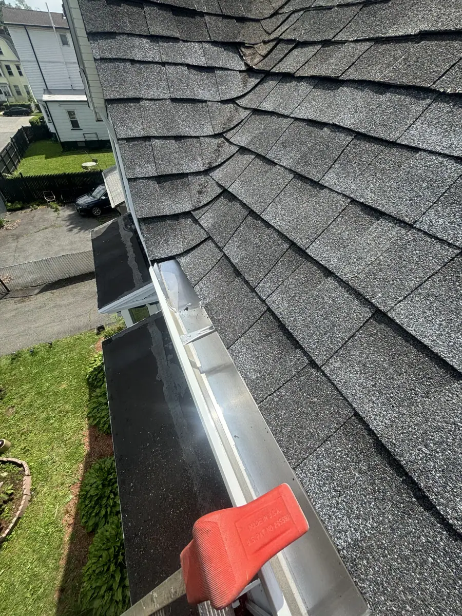 A new white gutter run fitted along the eaves of a freshly shingled roof