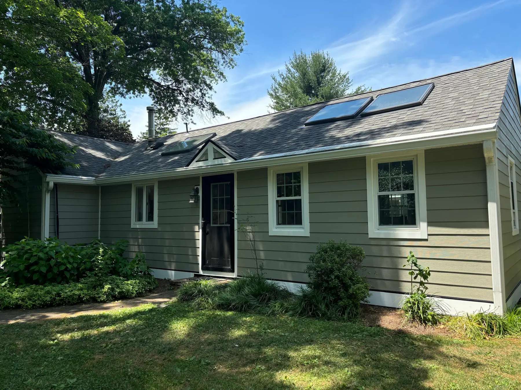 A single storey home finished with green siding and a new shingle roof with skylights