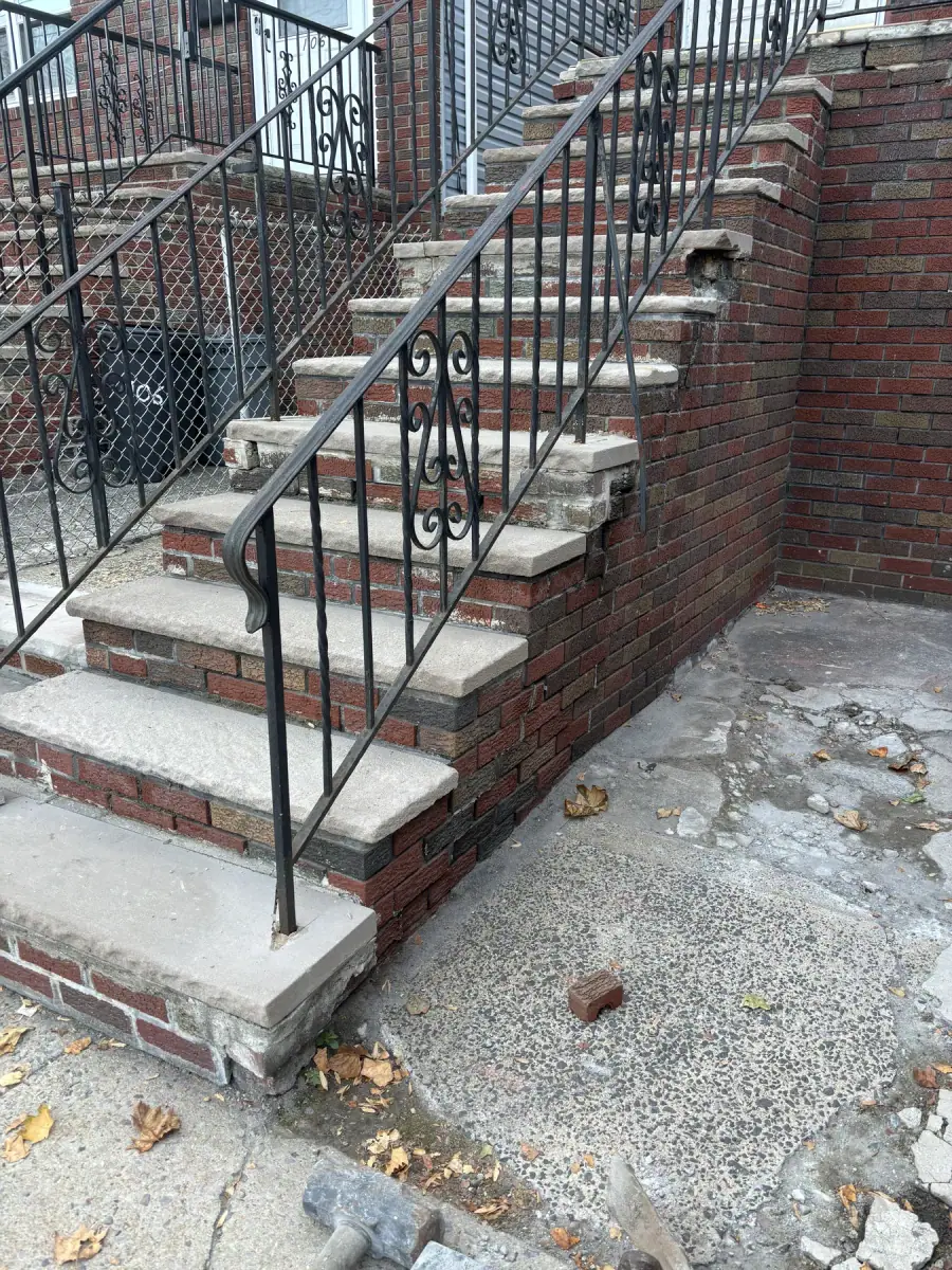 New brick steps with concrete treads and a black iron railing beside a brick retaining wall