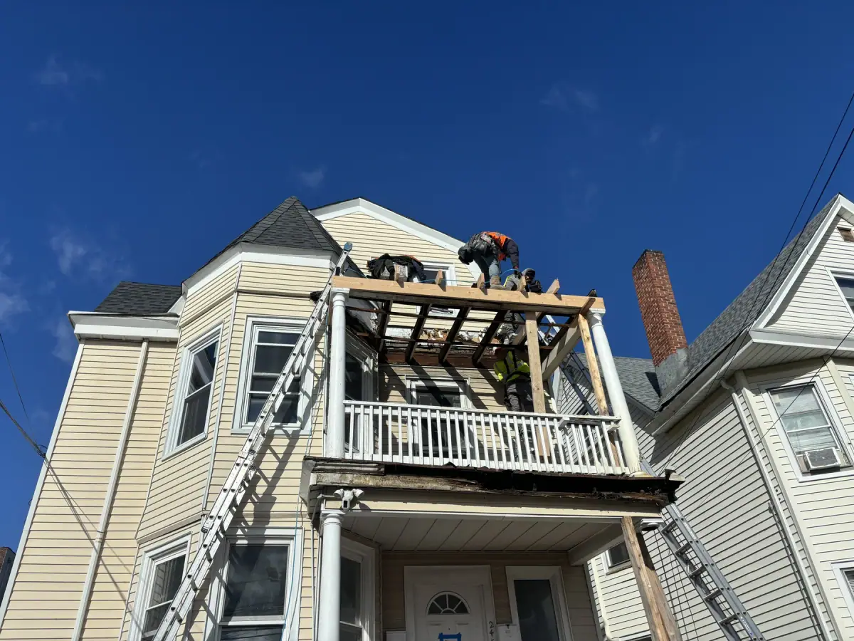 A crew member rebuilding the framing of a porch roof from a ladder