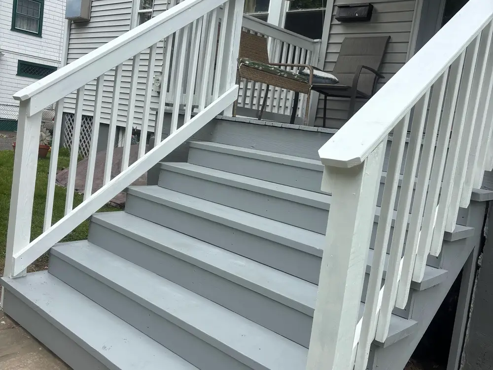 Rebuilt porch steps with grey treads and a white railing running down beside them