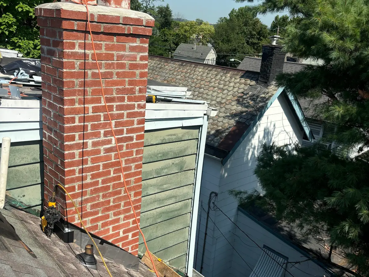 A rebuilt brick chimney with a new metal cap standing above a shingle roof