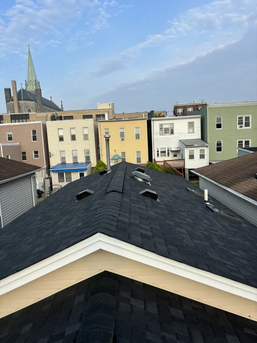 A finished dark shingle hip roof with a church spire and rooftops in the distance