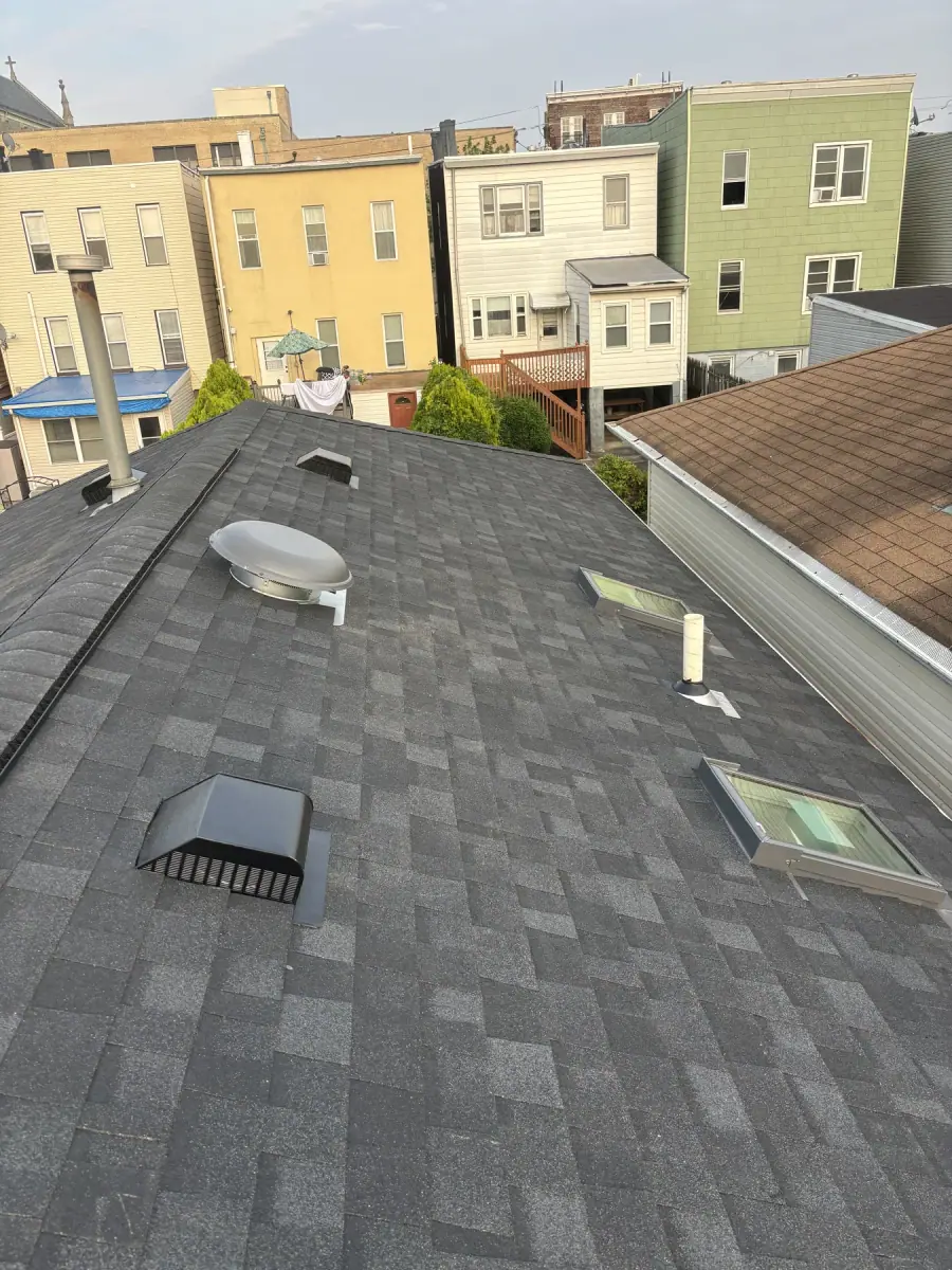A finished dark shingle roof with roof vents and a skylight set into it