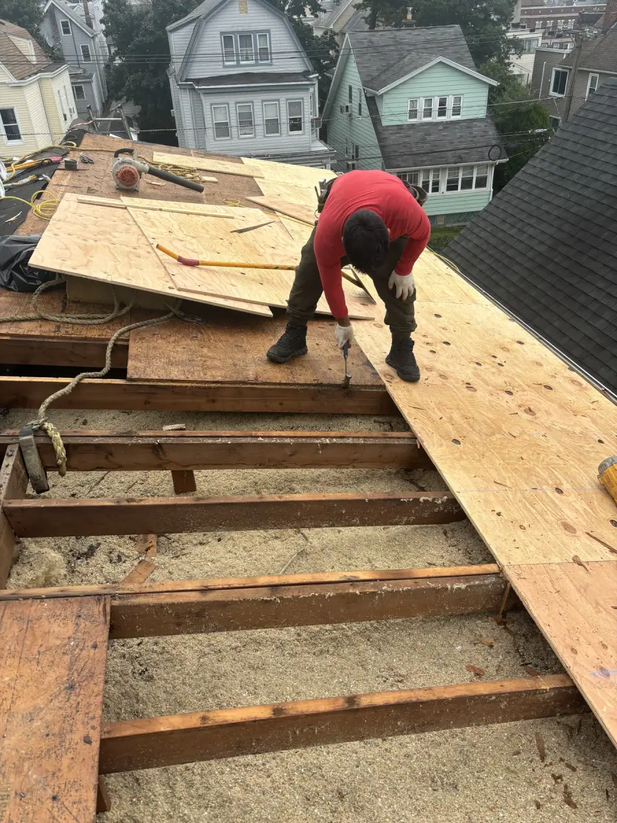 A crew member in a red shirt fastening new plywood decking over the exposed rafters