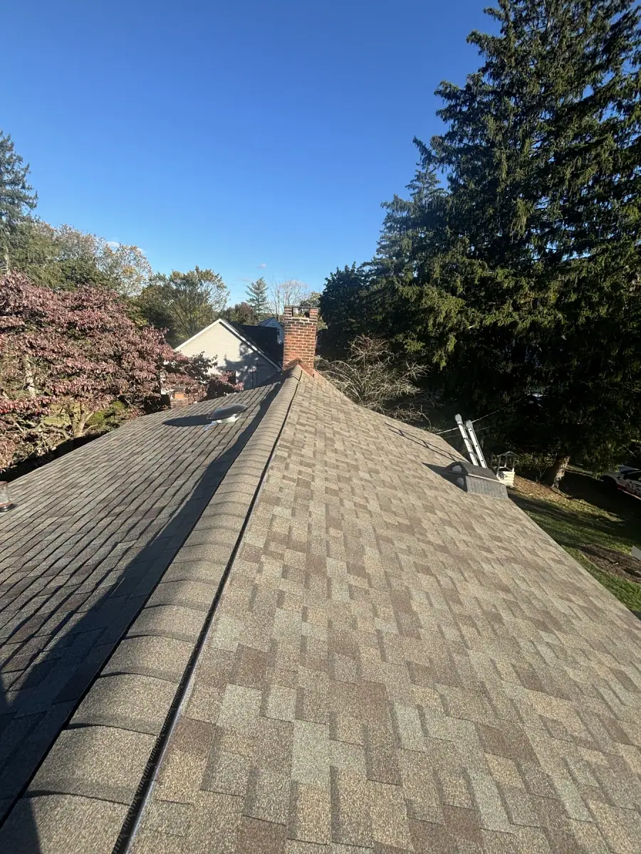 A long run of new shingles along a ridge, a brick chimney standing beyond it