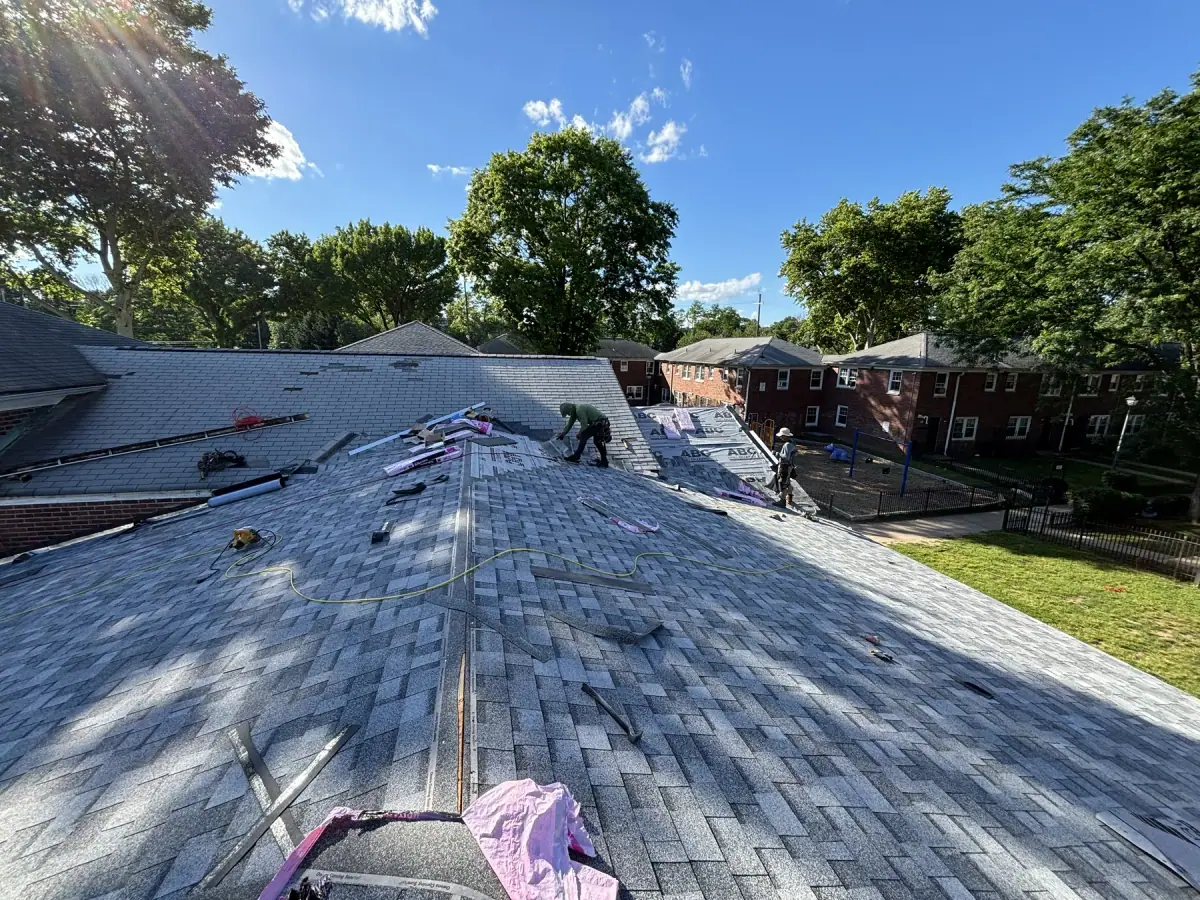 A long roof half shingled, the crew working at the far end above brick homes