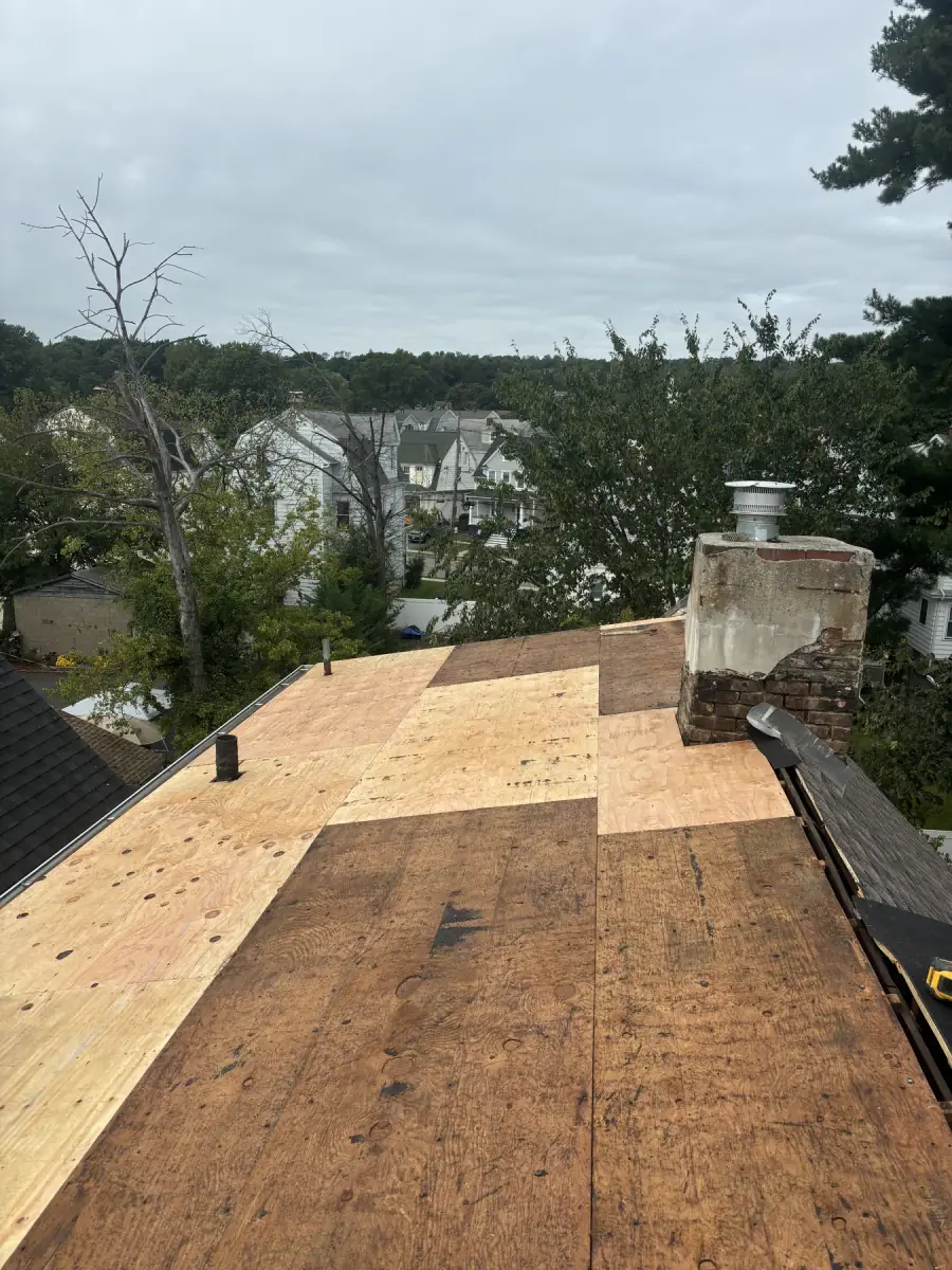New plywood decking laid across a roof up to the base of a brick chimney