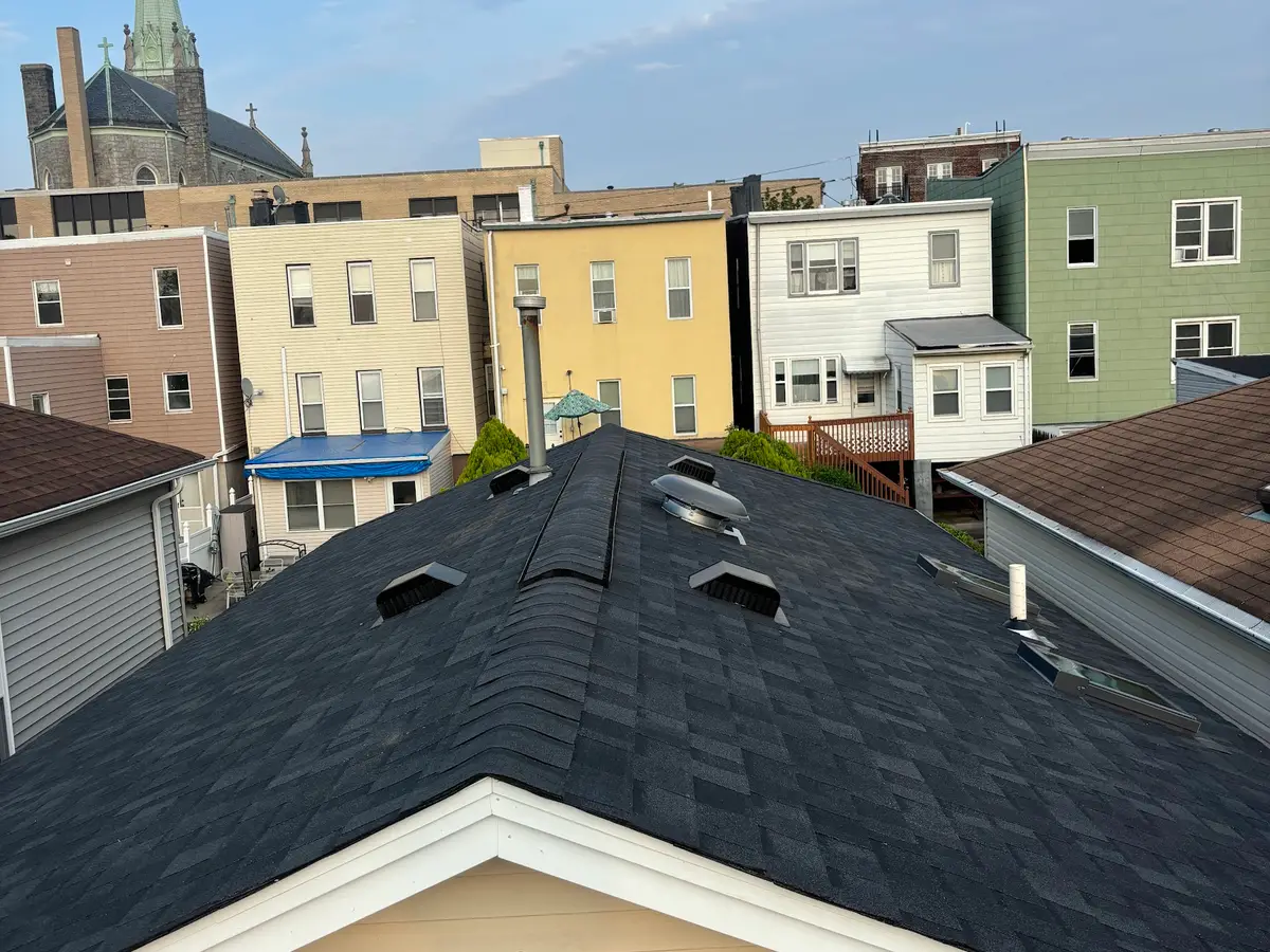 A finished dark grey shingle roof with ridge vents on a house in a row of homes in Orange, New Jersey