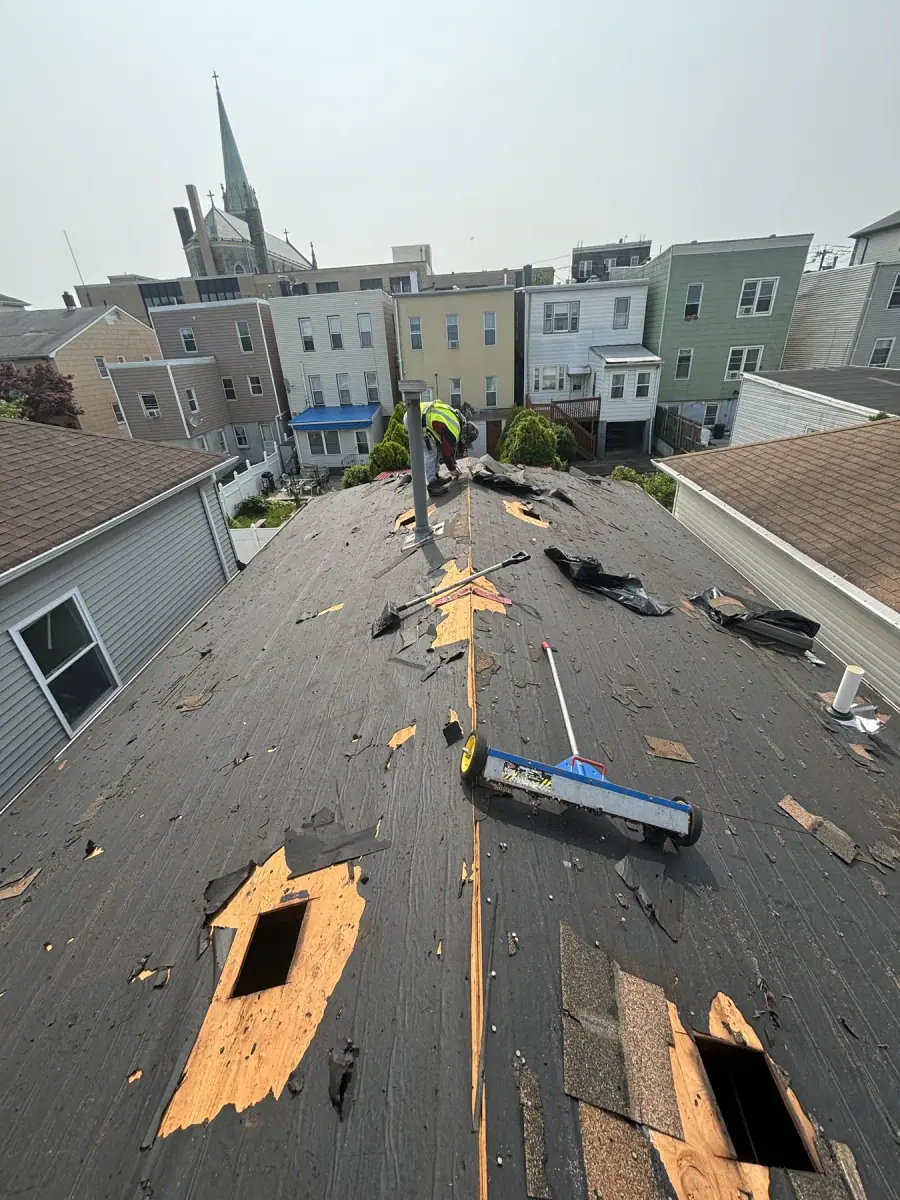 Old shingles being stripped from a roof, the bare deck showing through in patches