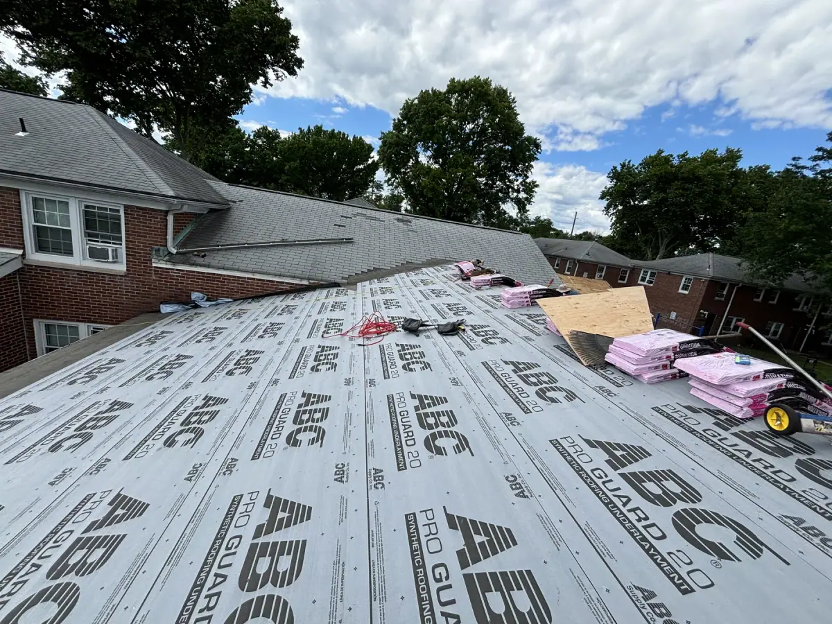 Synthetic underlayment rolled across a roof deck with bundles of shingles staged ready to lay