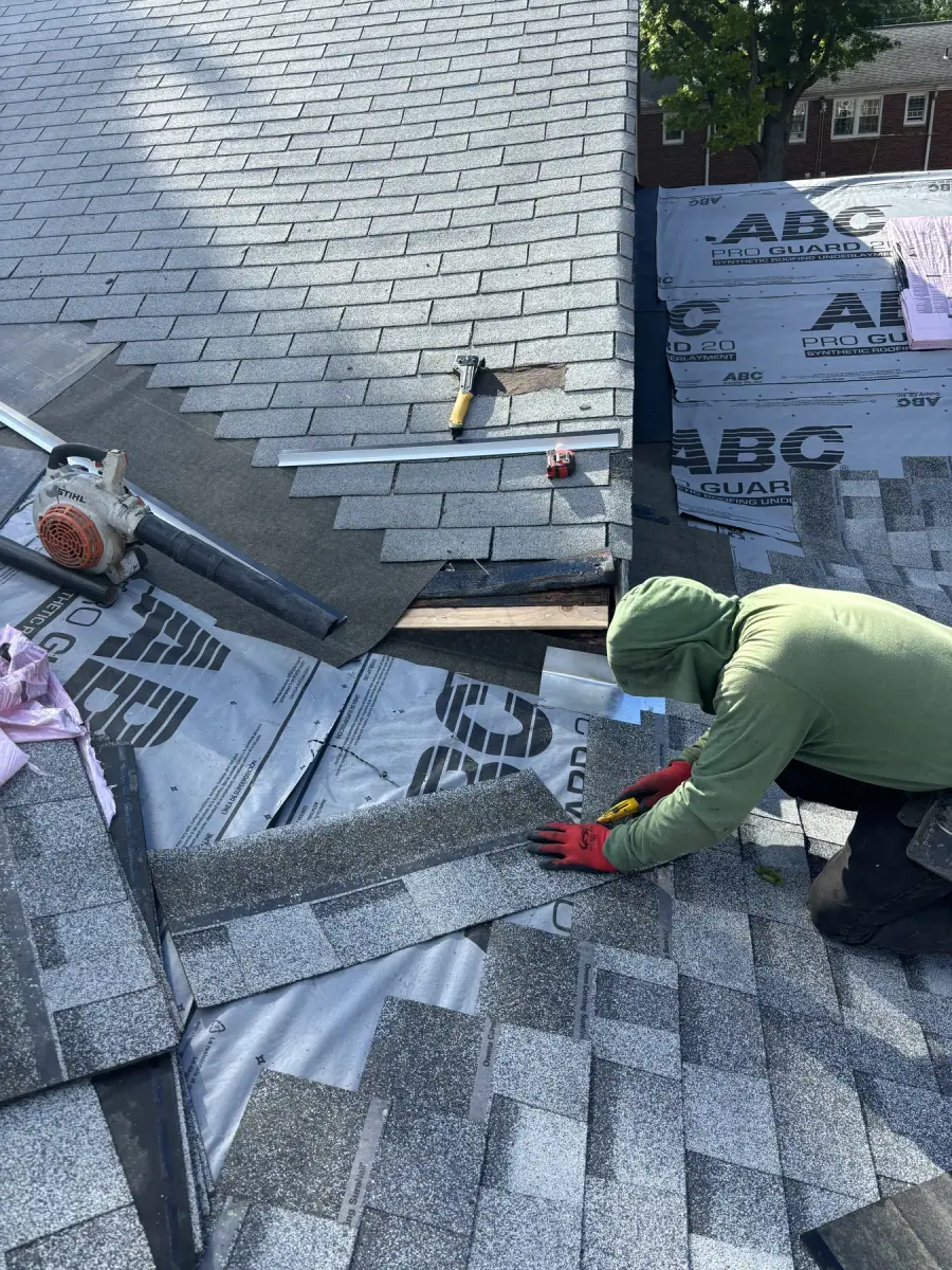 A roofer kneeling to lay a course of grey shingles over fresh underlayment