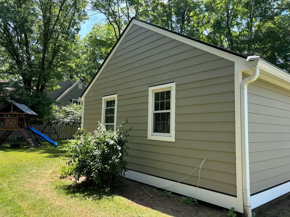 The side elevation of a house finished in sage green siding with white window trim