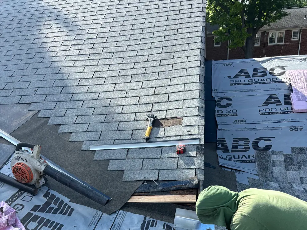 New shingles being nailed down over fresh underlayment, hammer in hand