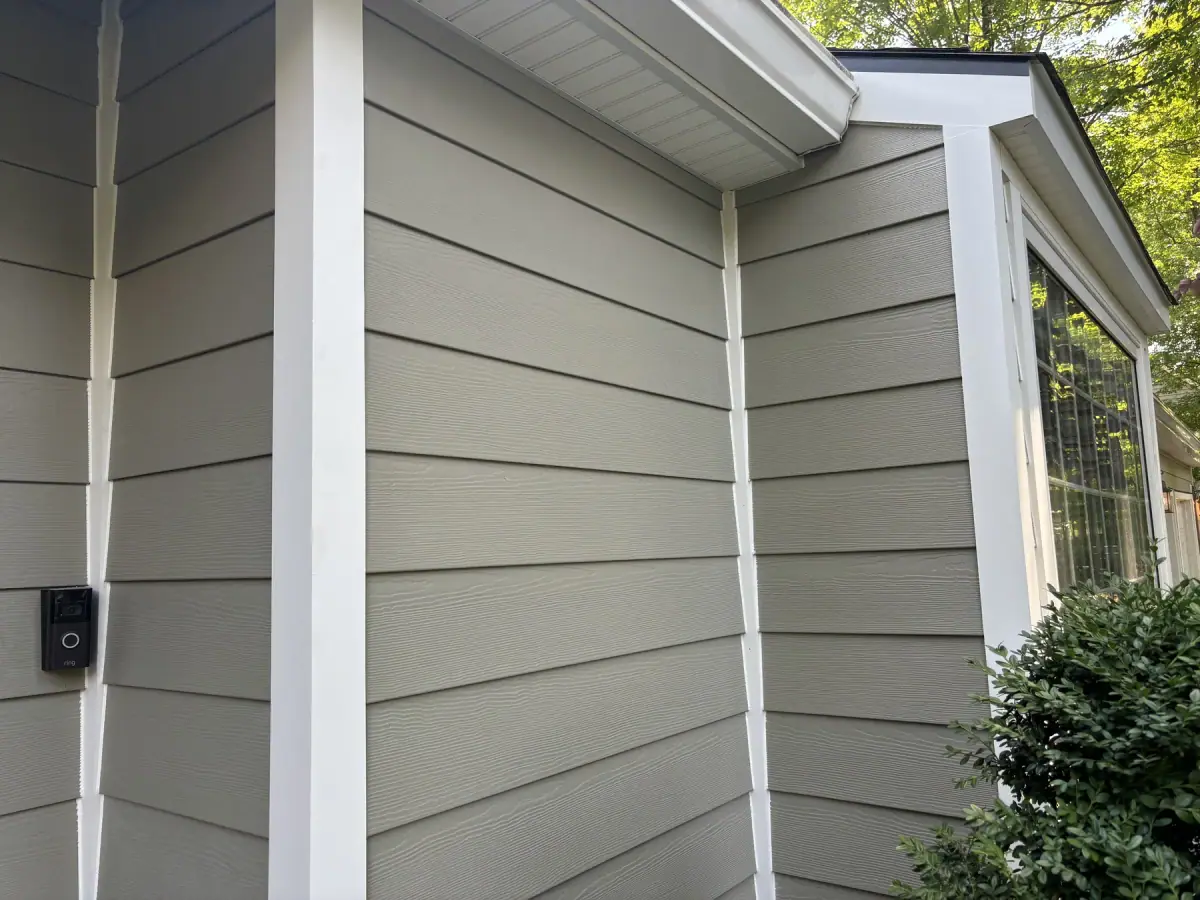 The corner of a house in new sage green siding with white trim boards and a new gutter