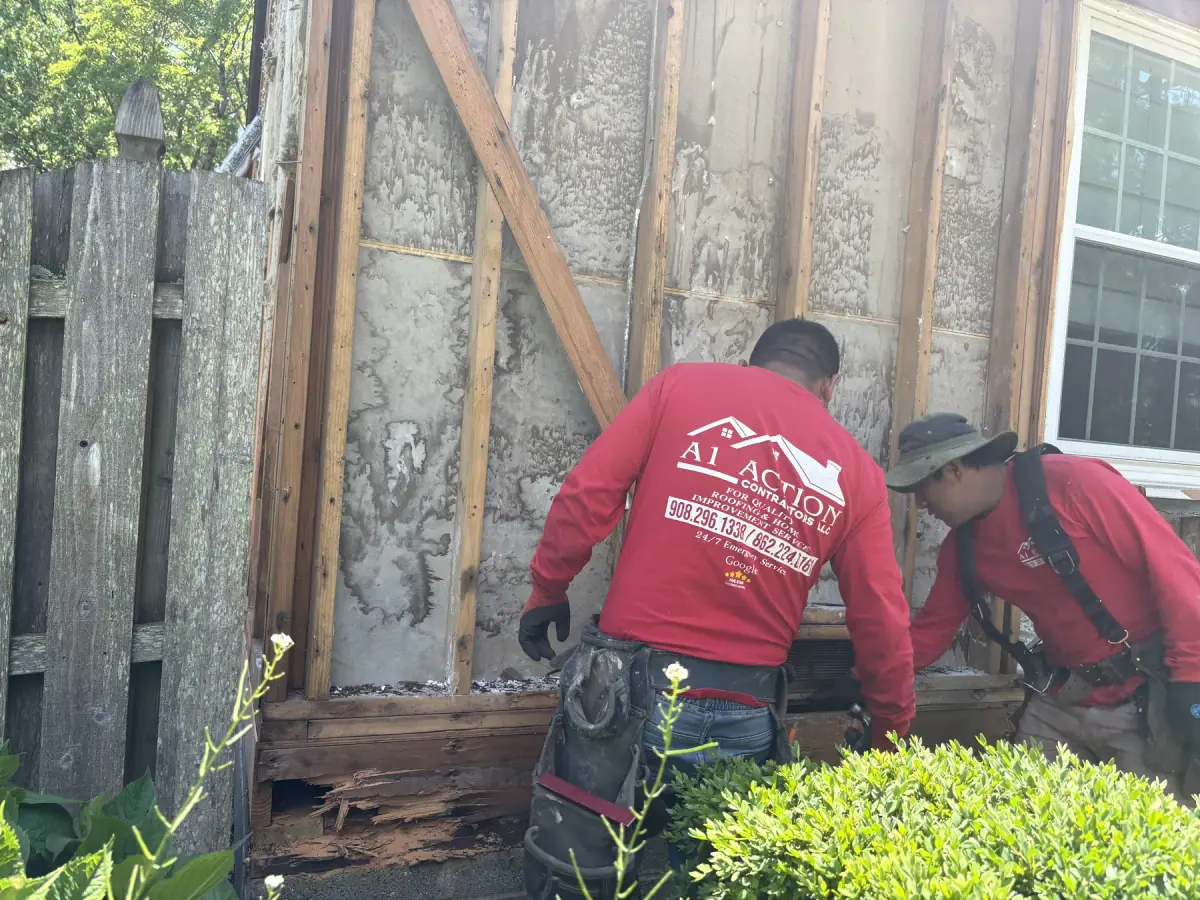 A crew member in a red A1 Action shirt working at a wall stripped back to studs and old boards