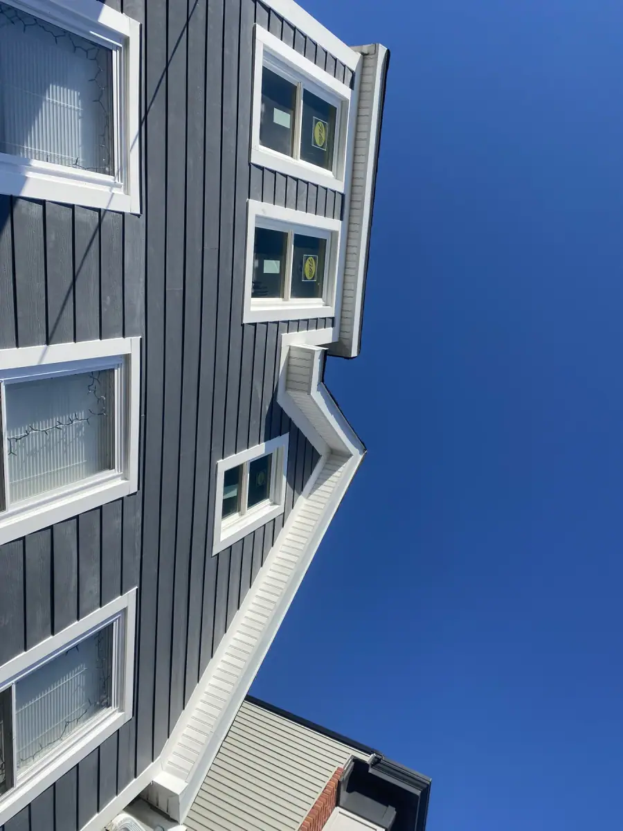 Dark navy siding with white trimmed windows, photographed looking up the wall against a blue sky