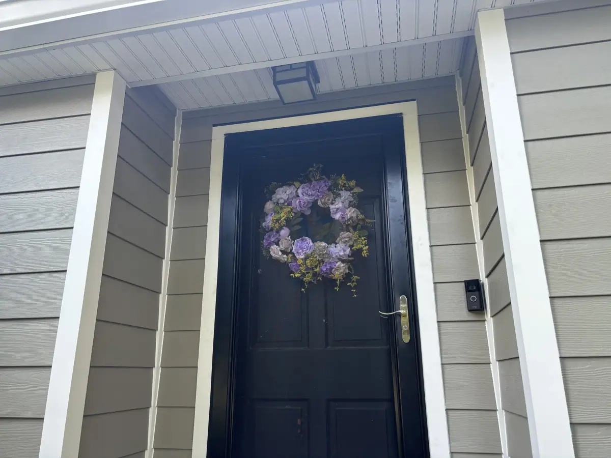 A dark front door framed by new sage green siding and white trim, a wreath on the door