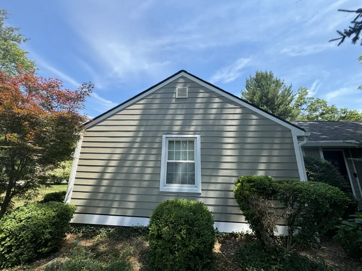 A gable end finished in new sage green siding with a white trimmed window and vent