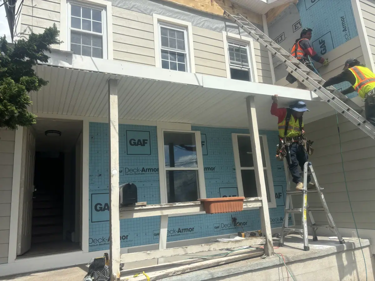 The front of a house in housewrap with crew working from ladders either side of the porch