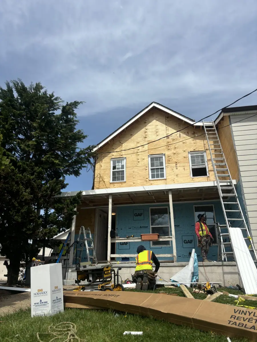 A two storey house wrapped in housewrap over new sheathing, ladders up to the porch roof